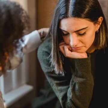 Picture of woman tapping shoulder of another female who looks depressed