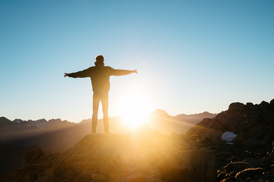 Man standing on top of a mountain as the sun rises with arms outstretched