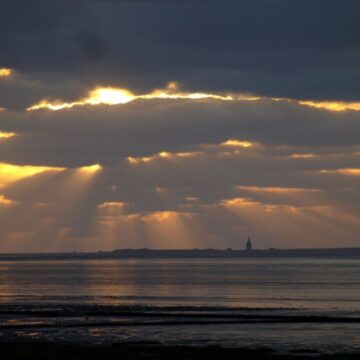 Sun peeking through clouds on a dark beach