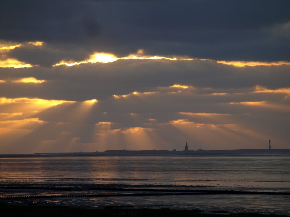 Sun peeking through clouds on a dark beach