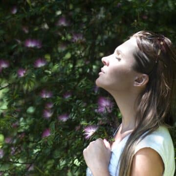 Woman with her eyes closed looking up at the sky with purple and green flowers in the background