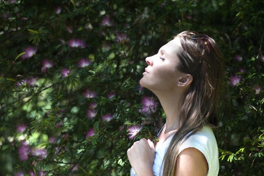 Woman with her eyes closed looking up at the sky with purple and green flowers in the background