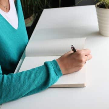 Woman in a teal blue sweater writing in a notepad