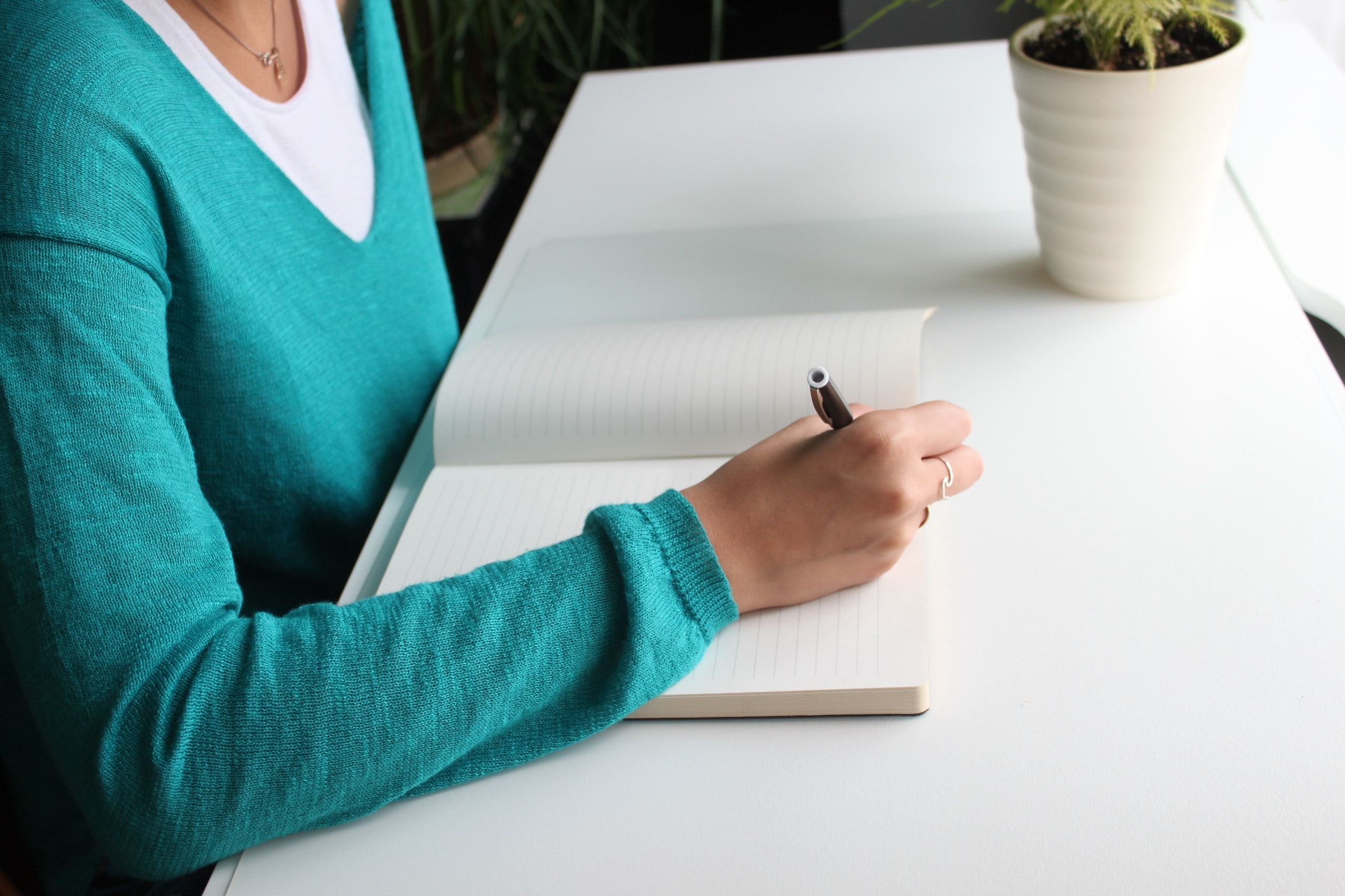 Woman in a teal blue sweater writing in a notepad