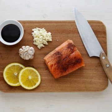 Wooden cutting board with butcher's knife, salmon, lemon, garlic and soy sauce