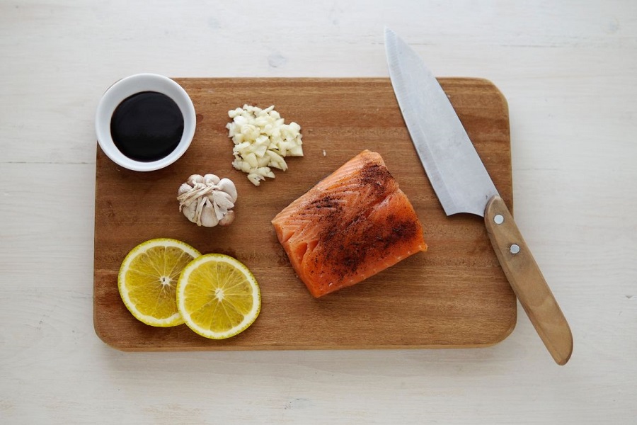 Wooden cutting board with butcher's knife, salmon, lemon, garlic and soy sauce