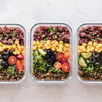 Three glass containers filled with lentils, rice, corn, olives, green onions, cucumbers and tomatoes