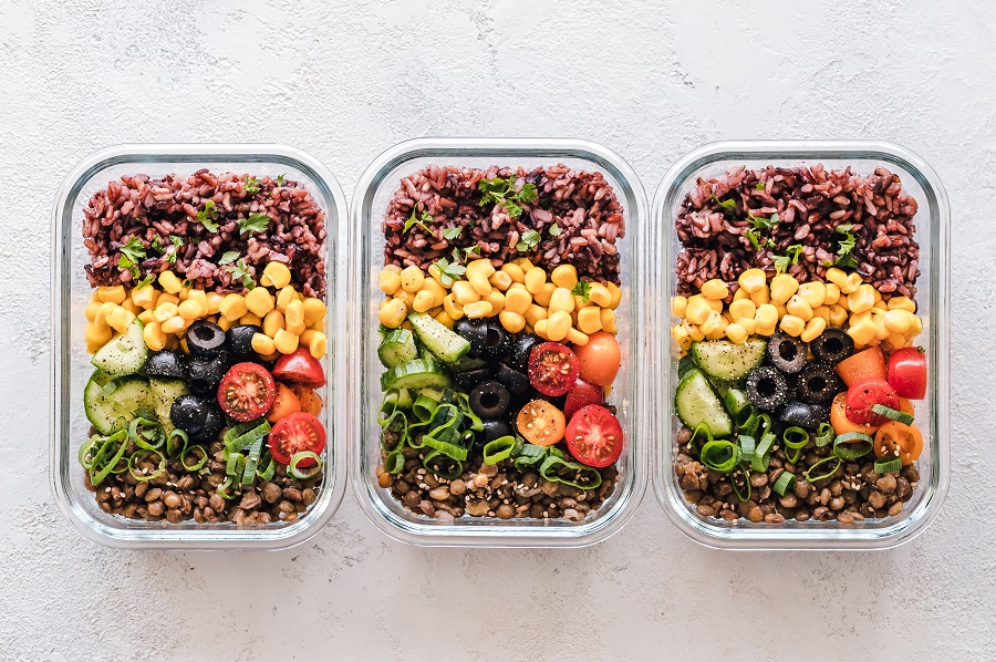 Three glass containers filled with lentils, rice, corn, olives, green onions, cucumbers and tomatoes