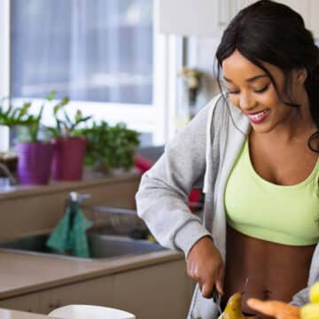 Woman in workout clothes smiling in kitchen preparing healthy food