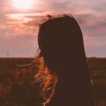 Girl standing in a cornfield during sunset