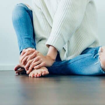 Woman sitting on a hardwood floor wearing a white sweater and ripped jeans