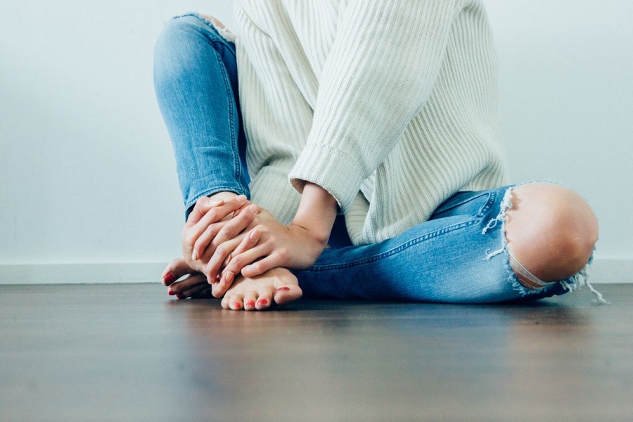 Woman sitting on a hardwood floor wearing a white sweater and ripped jeans