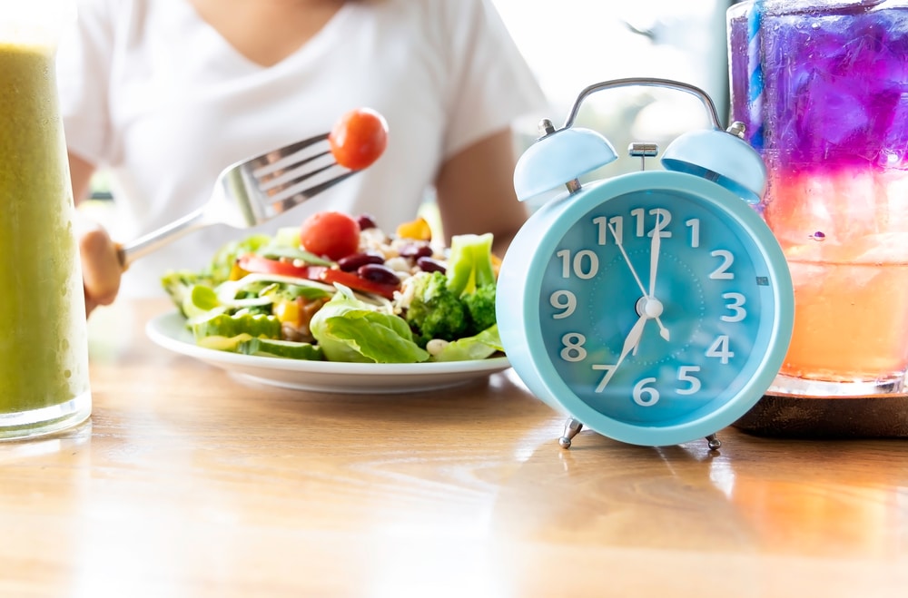 Person doing intermittent fasting and eating a salad next to an alarm clock
