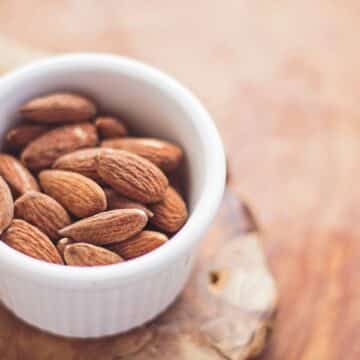 White ceramic bowl holding almonds on top of a wooden surface