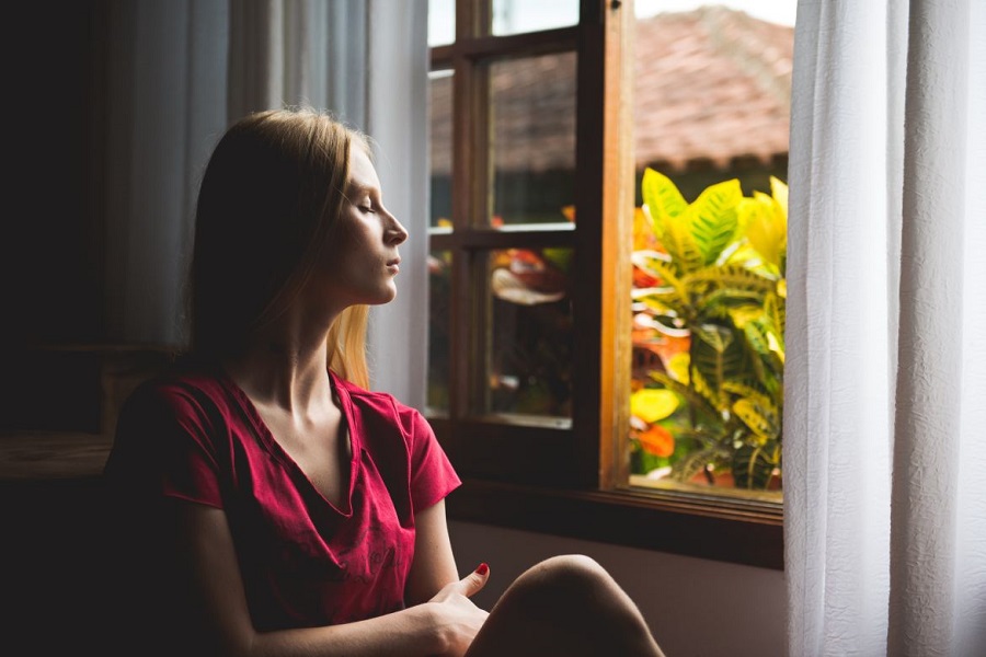 Woman sitting with her eyes closed, facing an open window