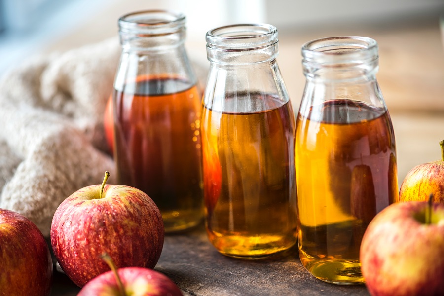 Apple juice in three glass containers surrounded by red and yellow apples and a sweater