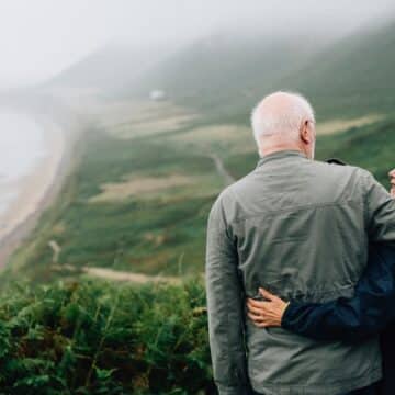 An older couple arm in arm looking at each other with greenery in the background