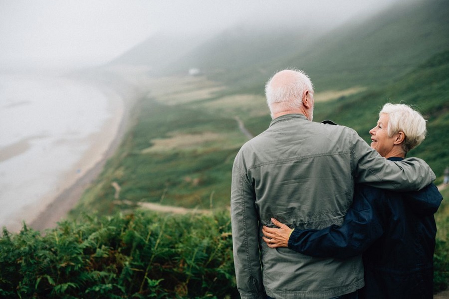 An older couple arm in arm looking at each other with greenery in the background