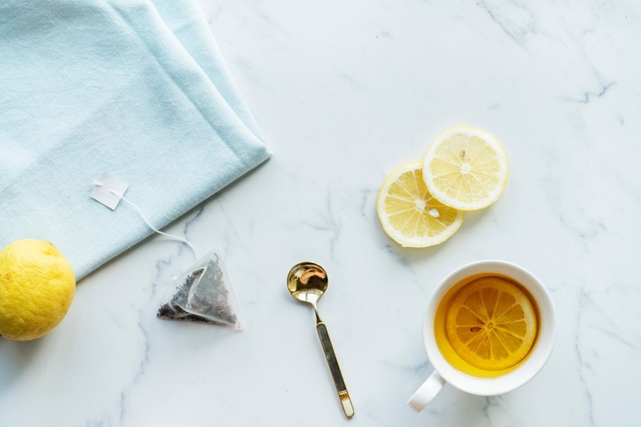 Tea in a white ceramic mug surrounded by a spoon, tea bag, and slices of lemon