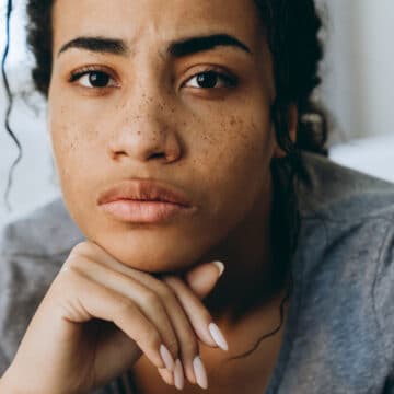 Serious woman with freckles, curly hair, and gray shirt.